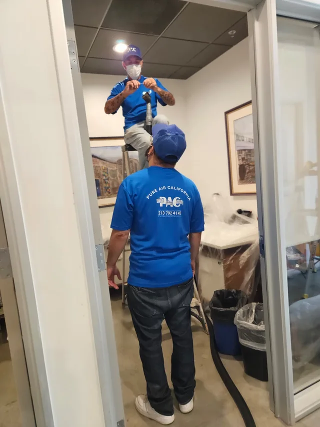 Two Pure Air California technicians working near a ceiling opening, with furniture protected below