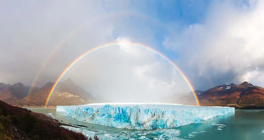 A double rainbow over a blue glacier and mountain lake