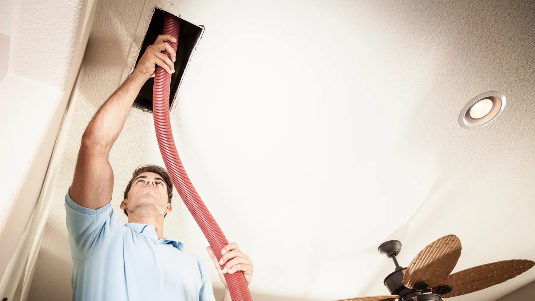 Technician using a hose to clean ceiling ductwork